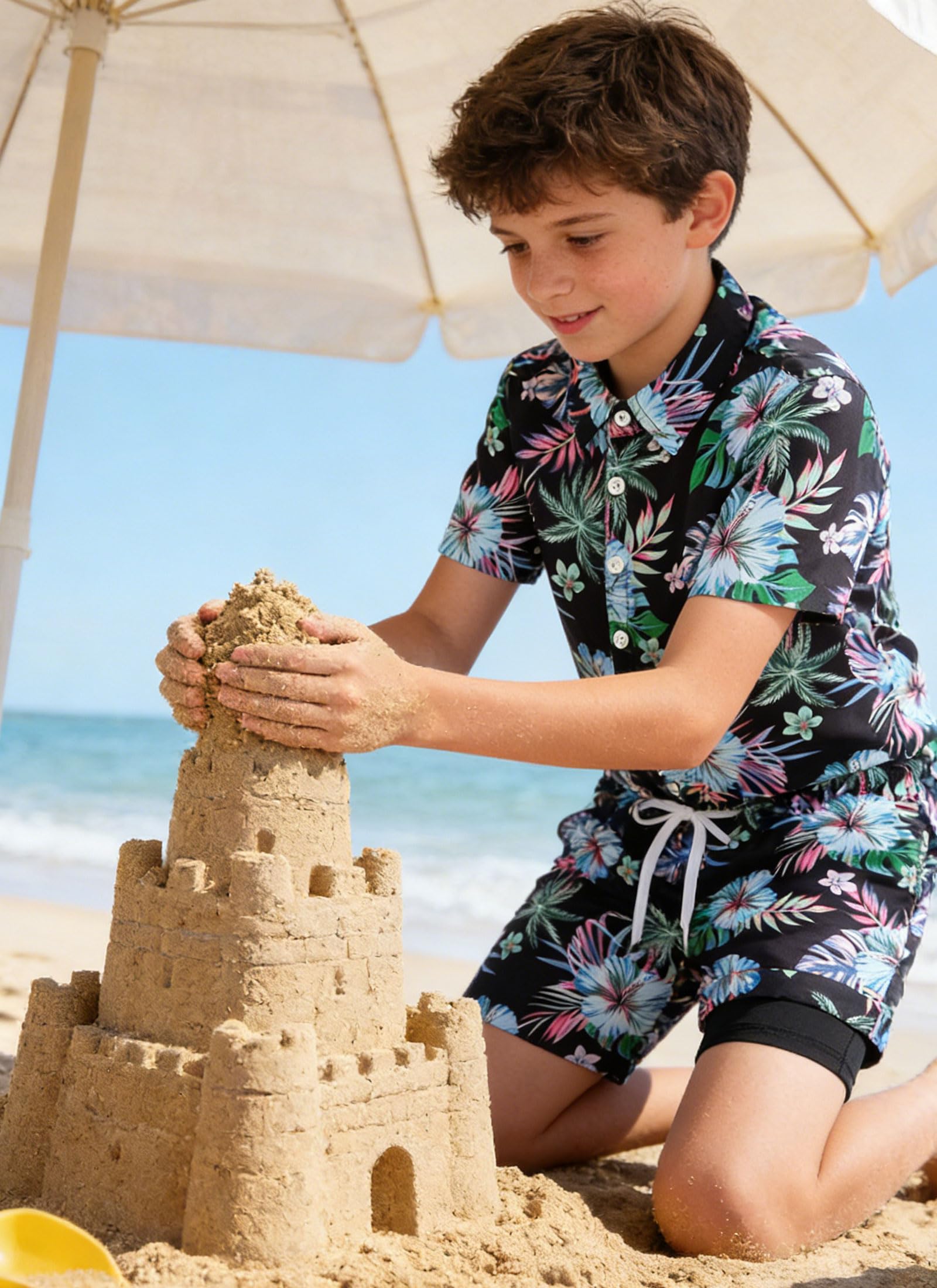 Boy wearing a Hawaiian shirt and swim shorts set while playing at the beach, perfect kids vacation wear.