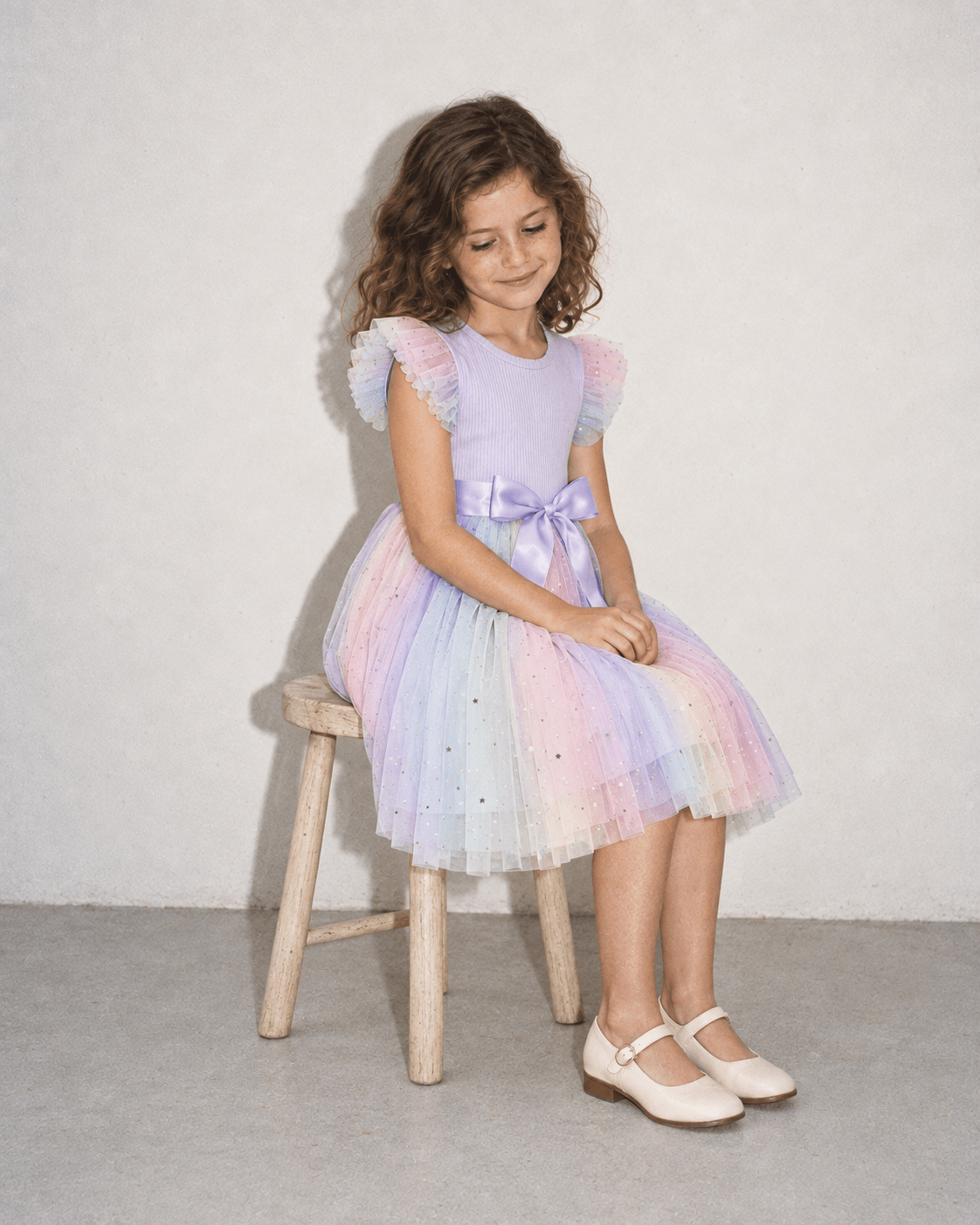 Girl sitting in a purple tulle dress, showing the soft layered skirt, comfortable fit and pastel party dress style for special occasions.