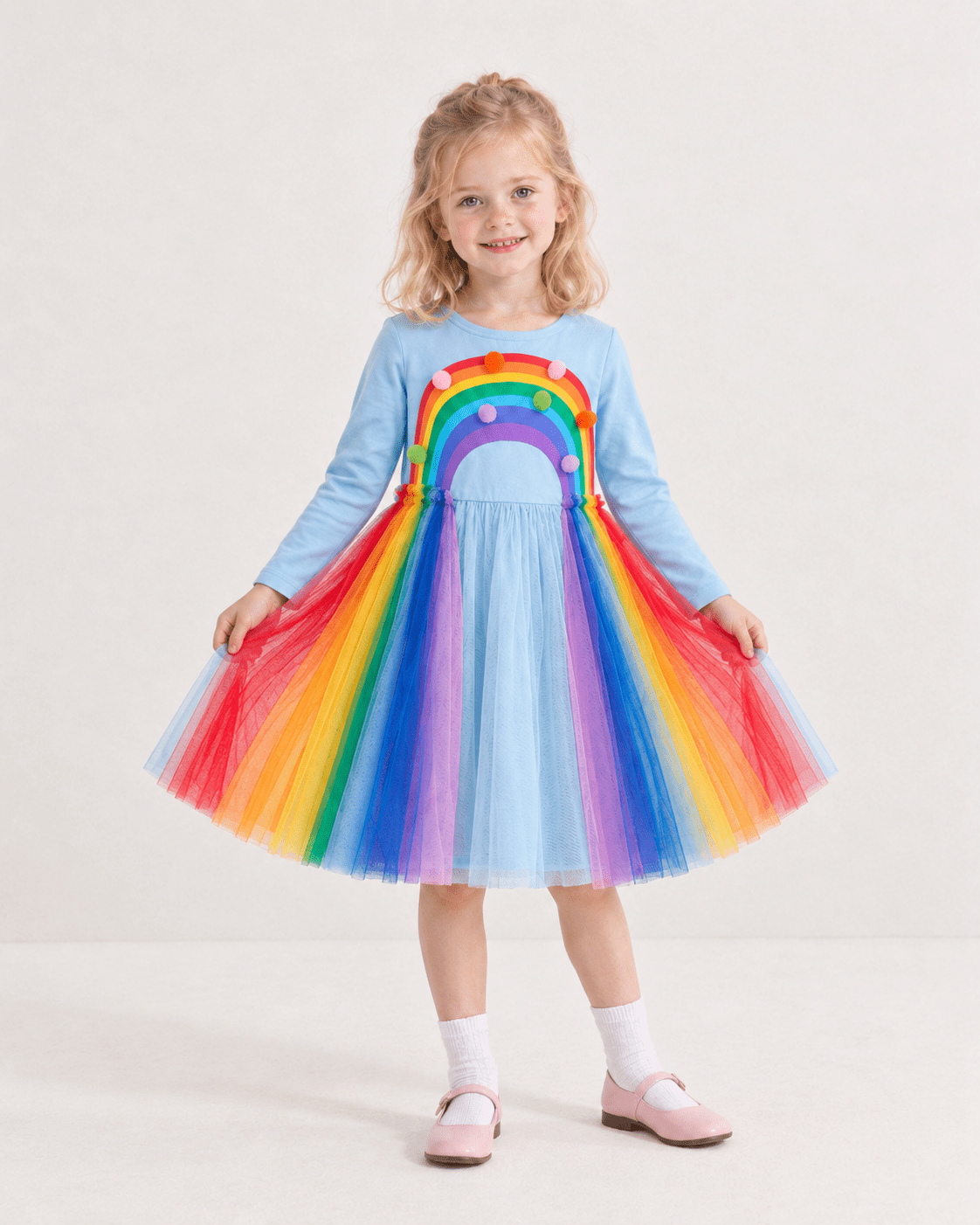 Girl wearing a rainbow tulle dress while holding the layered skirt, showing the colorful rainbow tulle layers, long sleeve design and princess-style silhouette.