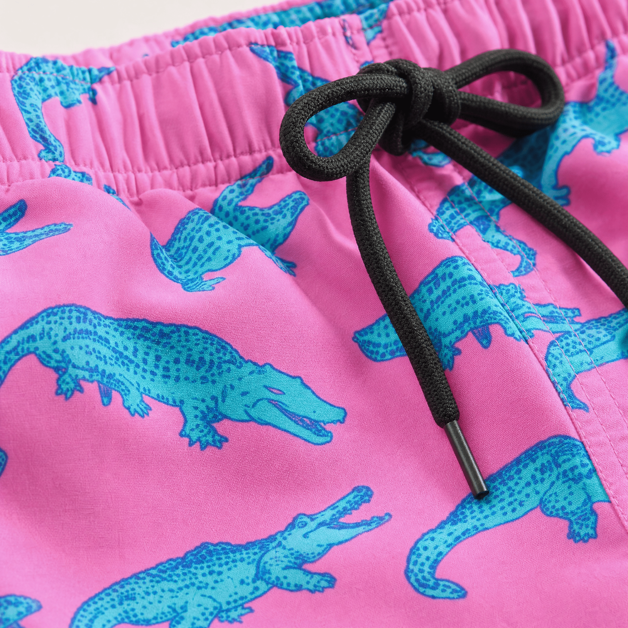 Nahaufnahme einer Badehose mit rosa Krokodilmuster, die ein farbenfrohes Ozeanmuster und ein leichtes Sommerstoffdesign zeigt.