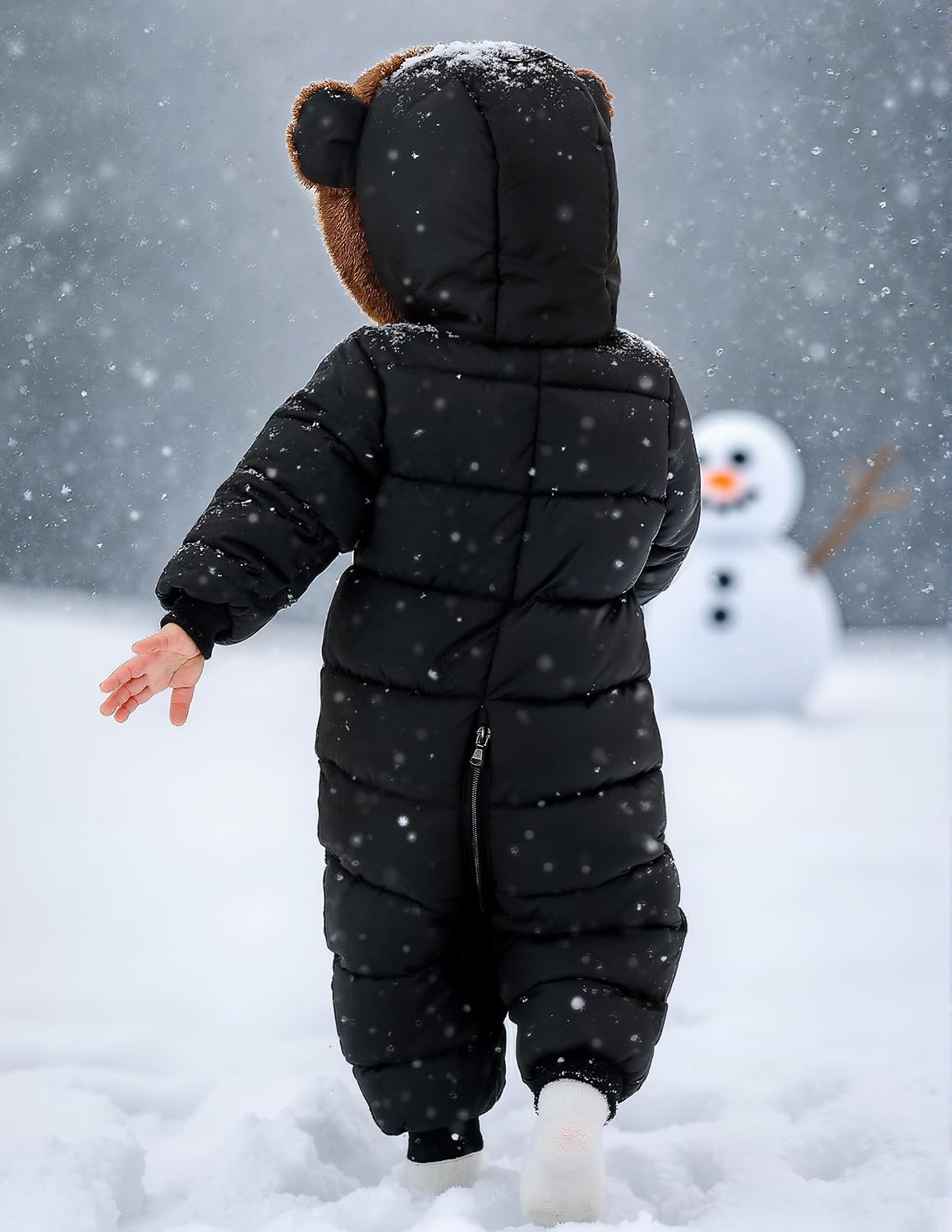 Back view of a toddler wearing a black one-piece snowsuit, showing the bear-ear hood and full-body quilted winter design.