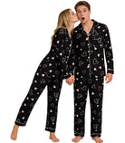 Couple standing together in matching black heart print pajamas, showing the button-down tops and relaxed full-length pants.