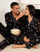 Couple dressed in coordinated Black Heart pajama sets, showing a comfortable matching look for home lounging and special occasions.