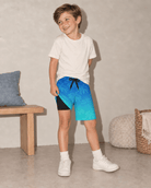 Boy wearing blue gradient palm tree swim trunks showing the built-in black liner, adjustable drawstring waist and comfortable two-in-one design.
