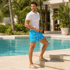 Man wearing Blue Palm 5.5 Inch swim shorts with green palm tree print while relaxing on a tropical beach.