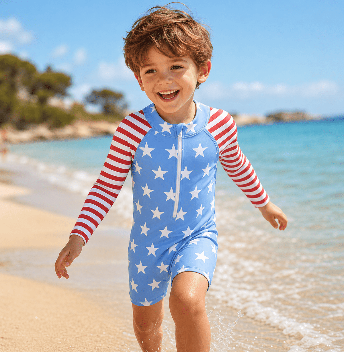 Toddler boy wearing a Blue Stars long sleeve rash guard swimsuit while walking by the beach, showing the comfortable one-piece swimwear fit.