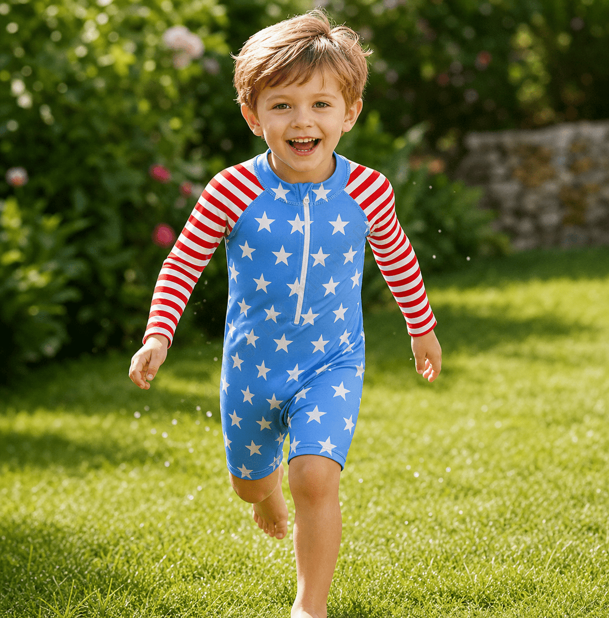Toddler boy wearing a Blue Stars printed rash guard swimsuit outdoors, showing the long sleeve design and easy zip front construction.
