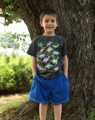 Boy wearing a black dinosaur print T shirt and blue shorts outdoors, displaying a comfortable everyday outfit for kids.