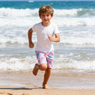 Boy wearing tropical palm tree swim shorts during a beach day, comfortable quick dry swim trunks for outdoor activities.
