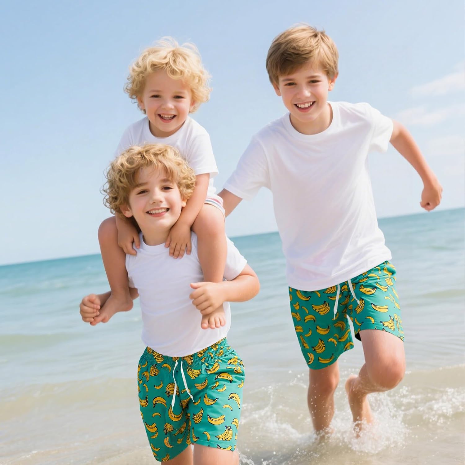 Kids wearing green banana print swim trunks running along the beach, showcasing lightweight quick-dry boys' swim shorts for summer vacations.