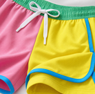 Detailaufnahme einer Jungen-Badeshorts in Farbblockoptik mit verstellbarem Kordelzug in der Taille, kontrastierenden Einsätzen und leichtem Sommerstoff.