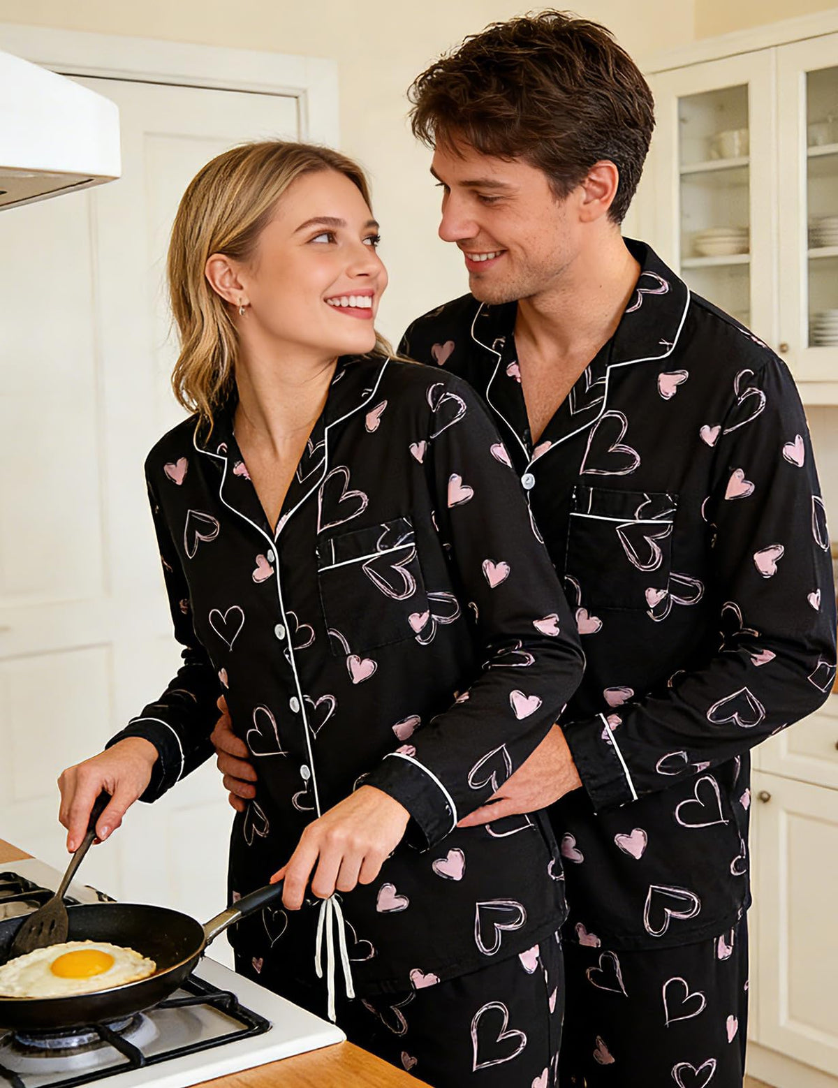 Couple wearing black heart matching pajamas indoors, showing the relaxed fit and coordinated two-piece sleepwear design.