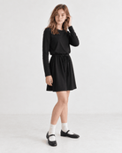 Girl wearing a black swing dress in a side pose, showing the flared A-line shape and long sleeve design.