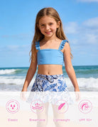 Girl wearing a blue bikini swim set with floral ruffle skirt at the beach, styled for swimming, vacations and summer seaside activities.