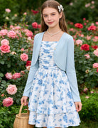 Girl wearing the Blue Floral dress and cardigan surrounded by blooming flowers.