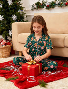Girl wearing a festive Christmas pajama set while opening gifts, showing comfortable holiday sleepwear for Christmas morning celebrations.
