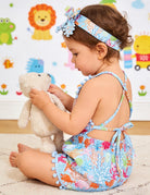 Young girl wearing a cute cotton blend romper dress with matching headband, perfect toddler outfit for playtime and summer activities.