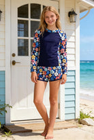Girl wearing a navy floral long sleeve rash guard swimsuit set outdoors, showing the comfortable fit, long sleeve design and matching swim shorts.