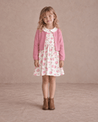 Girl wearing a pink floral dress and cardigan set in a front standing pose, showing the floral pattern, button cardigan and layered dress design.