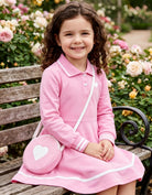 Girl wearing a pink long sleeve polo dress while sitting on a chair, showing the relaxed A-line silhouette and comfortable fit.