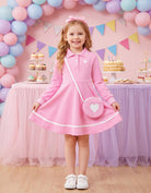 Girl wearing a pink long sleeve polo dress at a birthday celebration, stylish kids party outfit with a cute heart accessory.