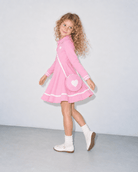 Girl wearing a pink long sleeve polo dress while walking, showing the side view, flared hem and matching heart shoulder bag.