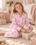 Girl sitting on the floor wearing a pink Santa Claus Christmas pajama set, showing the festive print top, matching pants and comfortable holiday sleepwear style.