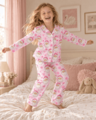 Girl standing on the bed wearing a pink Santa Claus Christmas pajama set, showing the full two piece sleepwear design and festive holiday pattern.