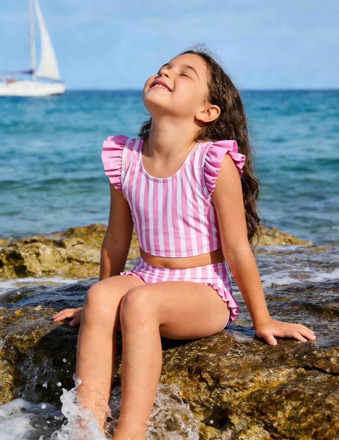 Girl wearing a pink striped ruffle bikini set while sitting by the ocean, showing a cute summer swimsuit for beach vacations.
