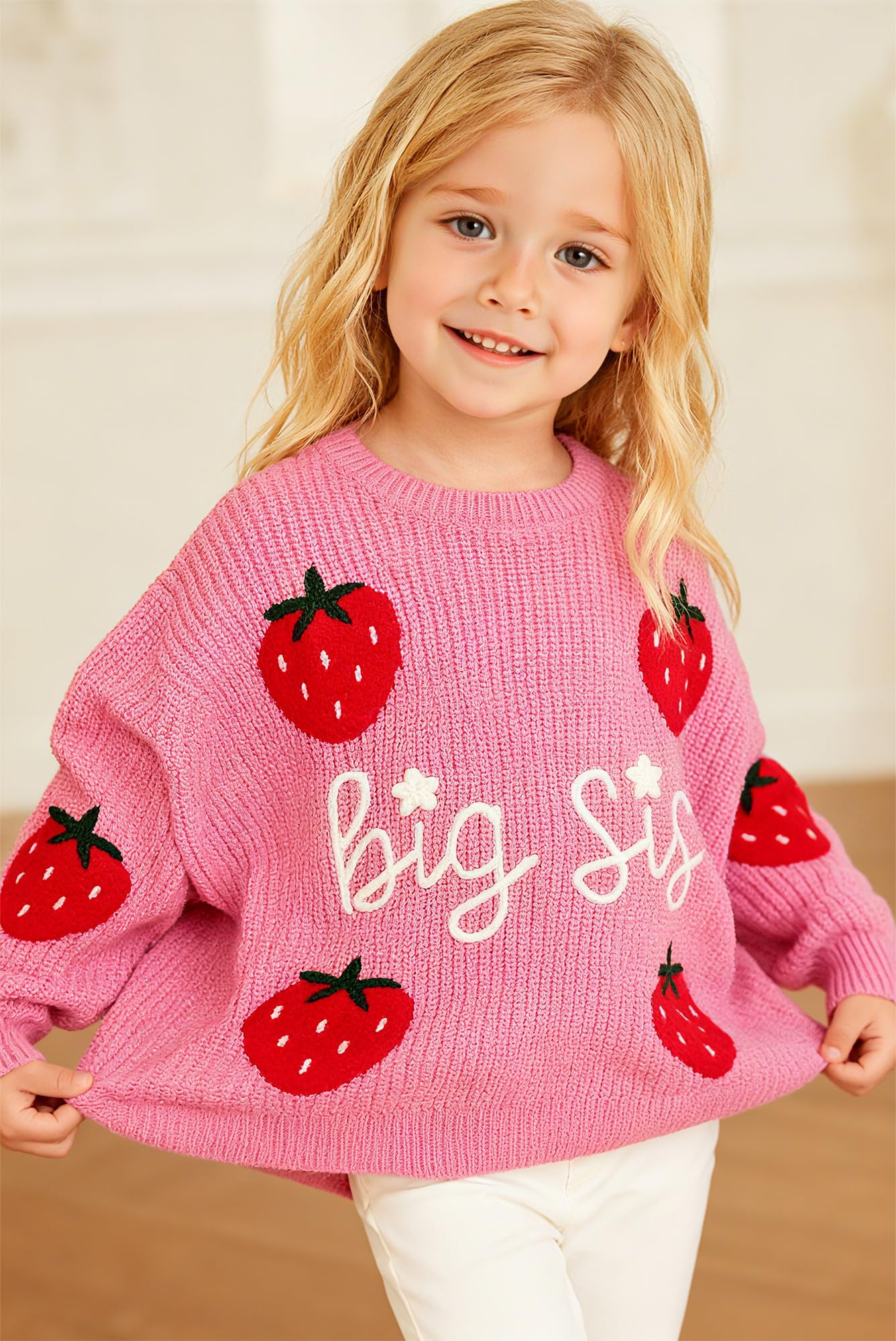 Girl wearing a raspberry pink Big Sis strawberry knit sweater, showing the cozy crew neck fit and playful sibling design.