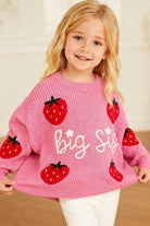 Girl wearing a raspberry pink Big Sis strawberry knit sweater, showing the cozy crew neck fit and playful sibling design.