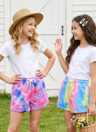 Two girls wearing colorful tie dye shorts outdoors, showing a comfortable summer outfit style for play, vacations and casual activities.