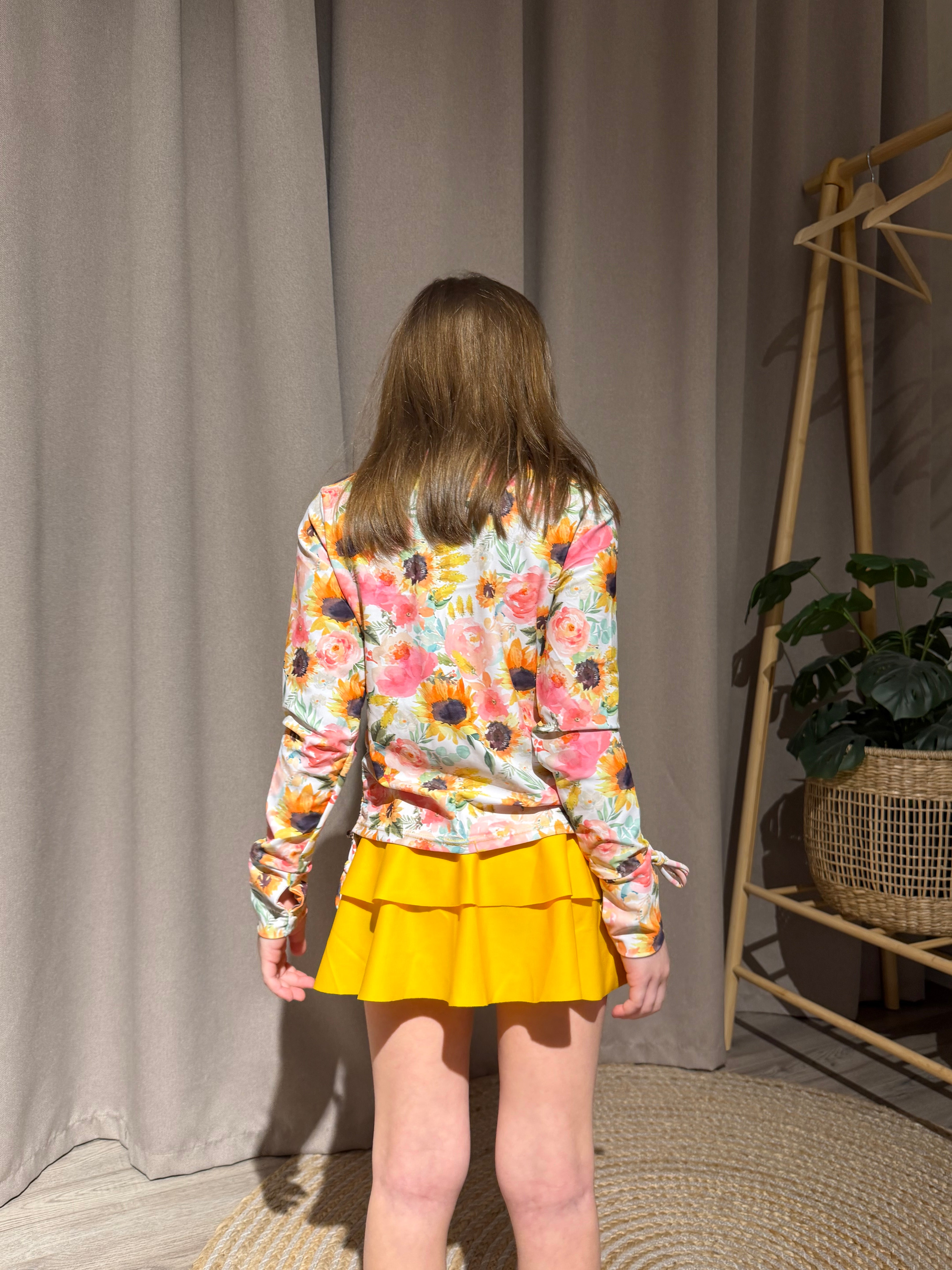 Back view of a girl wearing a Yellow Sunflowers long sleeve rash guard swimsuit set, showing the printed back design and matching swim skirt.