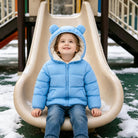 Child wearing a blue bear ear puffer jacket while sitting on a playground slide in snowy weather, styled for outdoor winter play.