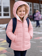 Girl wearing a pink hooded puffer jacket with a backpack outside school on a snowy day, styled as cozy winter outerwear for daily wear.