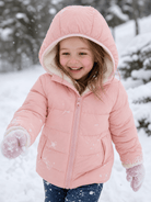 Girl wearing a pink hooded puffer jacket while playing in the snow, showing a warm quilted winter coat for outdoor cold-weather activities.