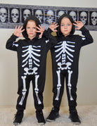 Kids wearing glow in the dark skeleton costumes together, showing the full-body Halloween outfit style for parties and trick or treating.