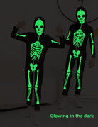 Kids wearing skeleton jumpsuits in the dark with glowing green bone prints, showing the luminous Halloween costume effect.