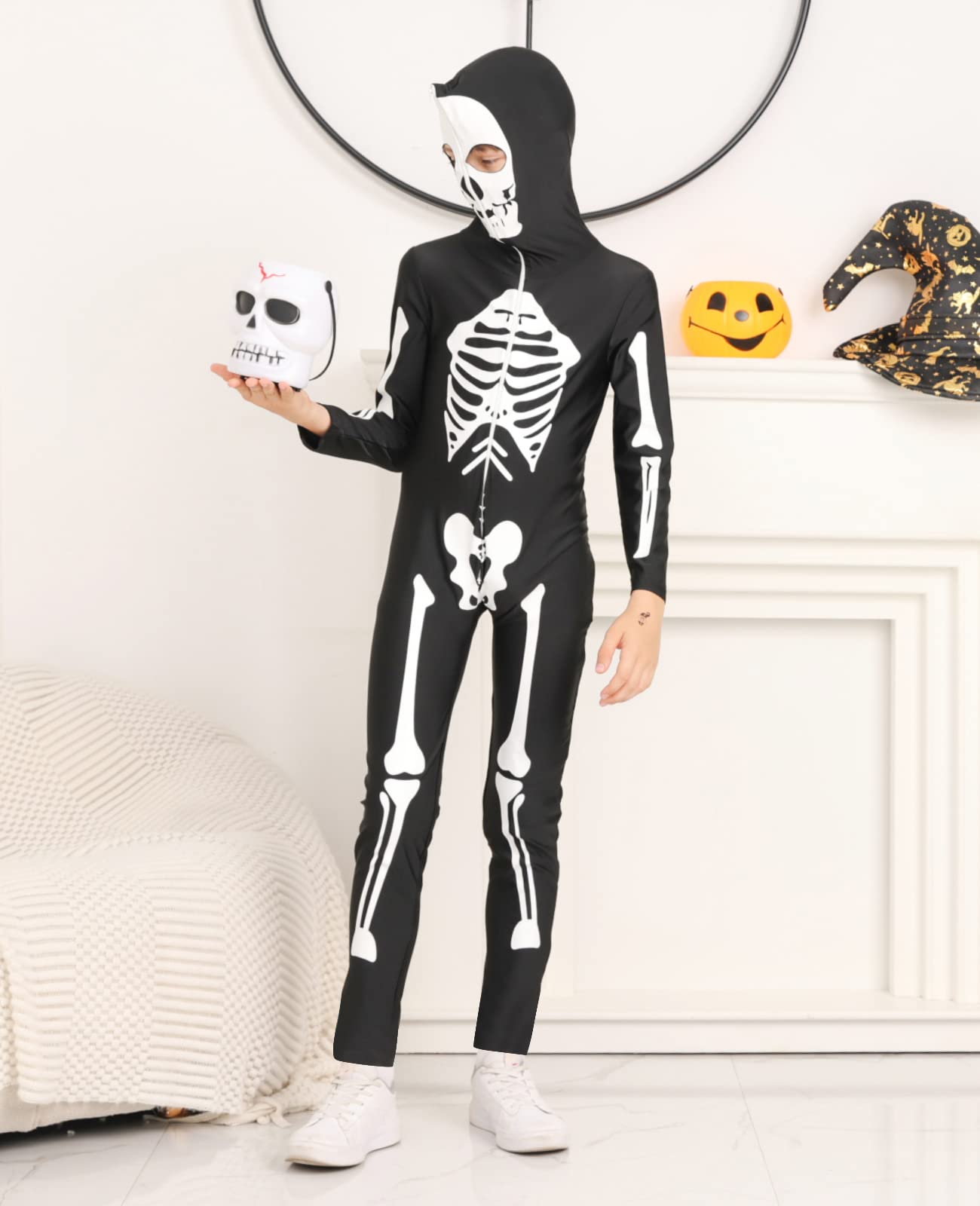 Child wearing a black skeleton jumpsuit indoors, showing the full-length hooded costume fit and printed bone design.