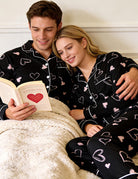 Couple wearing matching black heart pajama sets while relaxing together at home, styled for cozy nights and comfortable lounging.