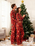 Couple wearing matching red plaid Christmas pajamas beside a decorated Christmas tree during holiday season