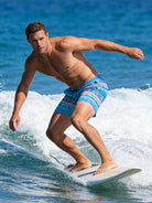 Man surfing in blue geometric print 2-in-1 swim trunks with a stretch compression liner for flexible movement on the water.