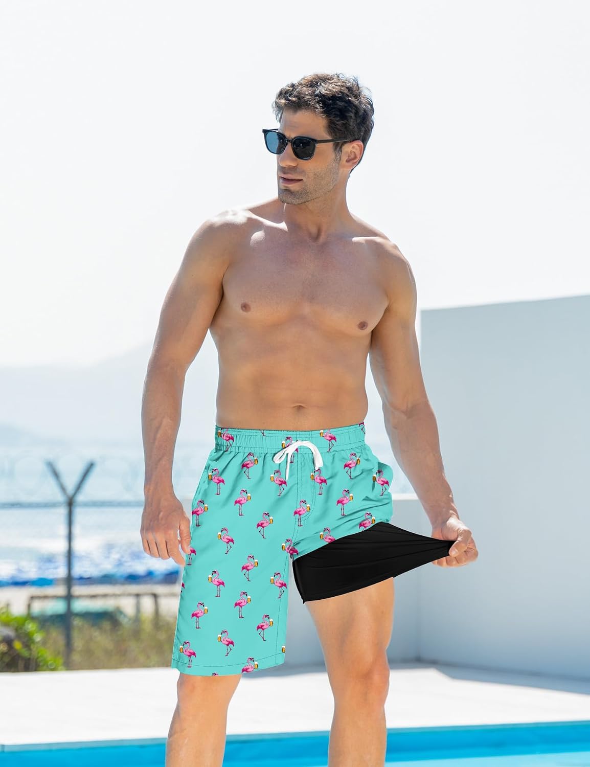 Man wearing blue flamingo swim trunks while stretching the black compression liner to demonstrate its flexible supportive design.