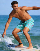 Man surfing in green flamingo 2-in-1 swim trunks, showing comfortable movement for surfing and summer water activities.