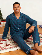 Man wearing navy plaid pajamas preparing Christmas gifts beside a decorated Christmas tree