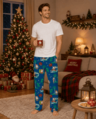 Man standing in Santa's Vacation pajama pants in a decorated Christmas room, showing the full-length fit and colorful holiday print.