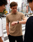 Man wearing a khaki textured knit polo shirt while checking his watch, styled for a clean and versatile smart casual look.