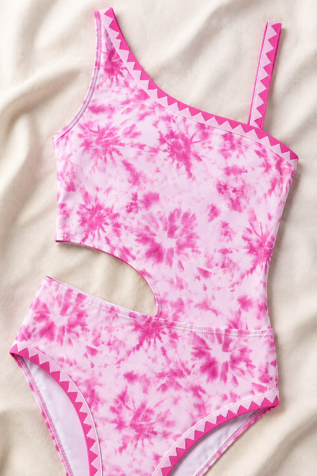 Close-up flat lay of the Pink Bloom one piece swimsuit showing the asymmetrical neckline, side cutout, pink printed fabric and contrast trim details.