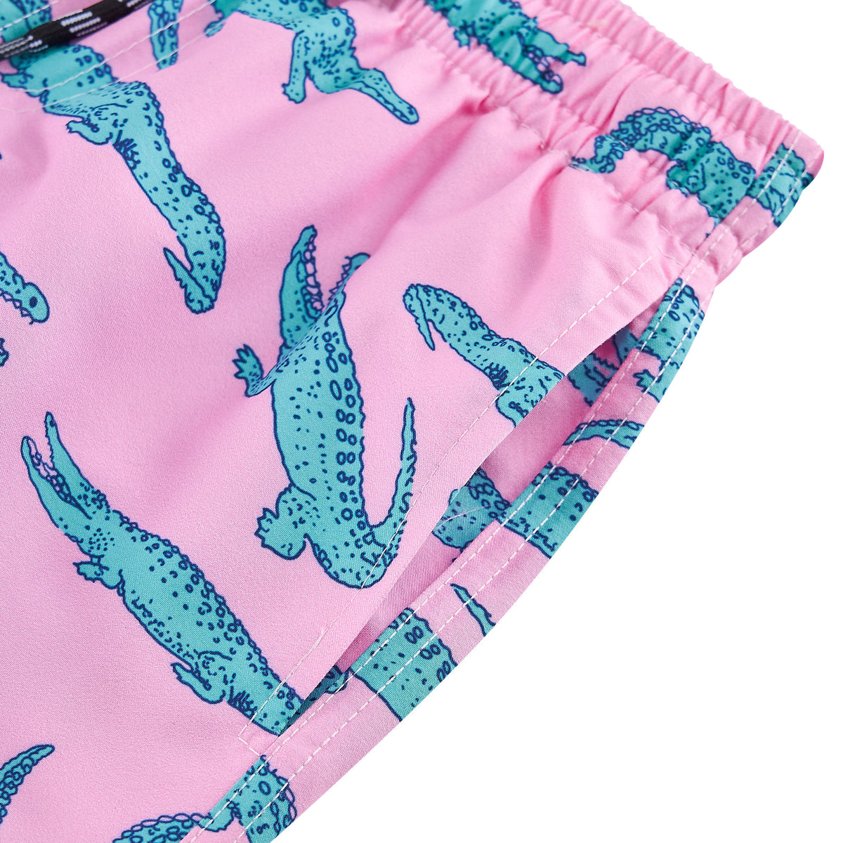 Close-up of pink crocodile swim shorts showing the side pocket opening, stitching details and teal crocodile pattern on pink fabric.