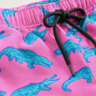 Close up of pink crocodile print swim trunks showing colorful ocean pattern and lightweight summer fabric design.